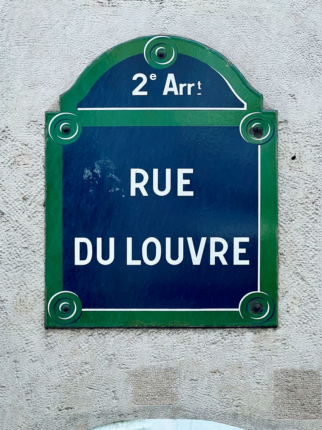 Street sign mounted on a weathered stucco wall.