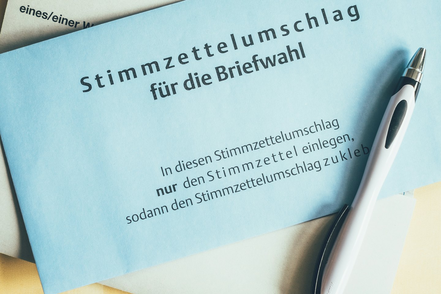 Blue mail-in voting envelope with a pen on a yellow surface.