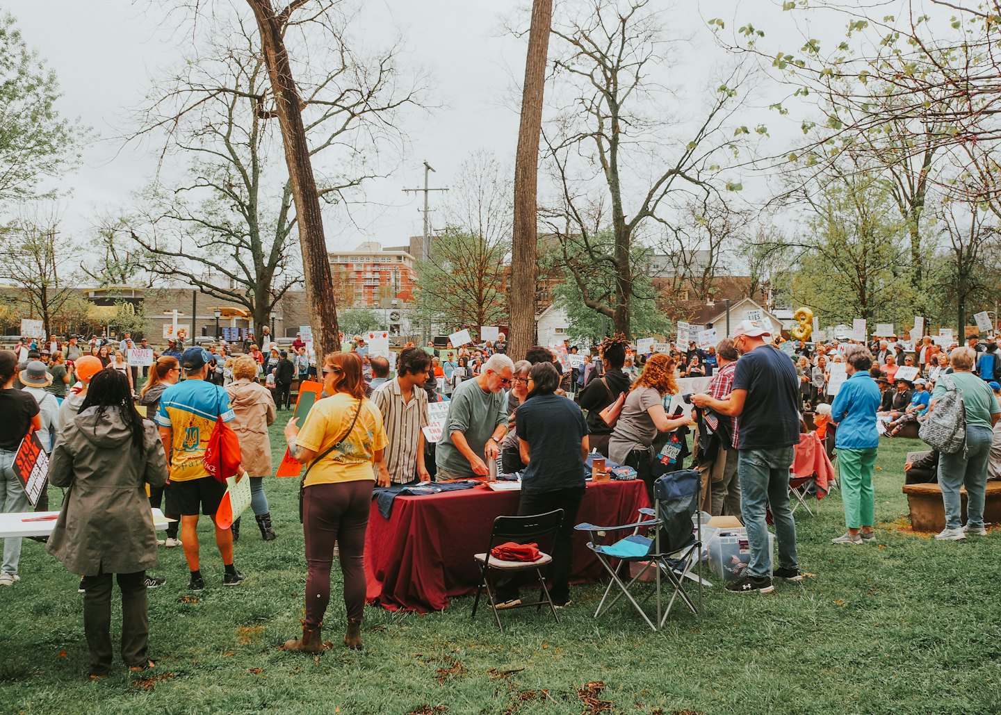 A group of protesters gathers in a park with signs.